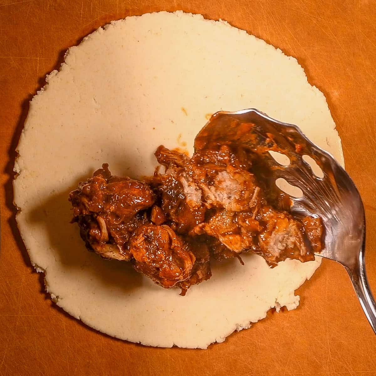 Add seasoned carnitas meat to a a piece of empanada dough.