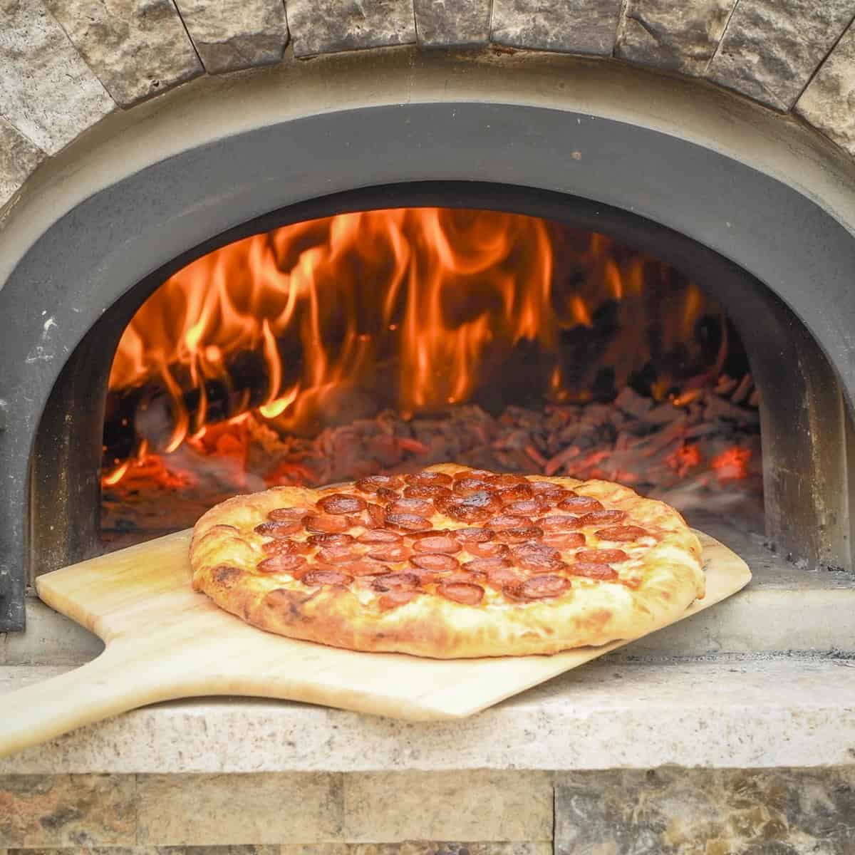 Cooked pepperoni pizza coming out of a wood-fired ovfen.