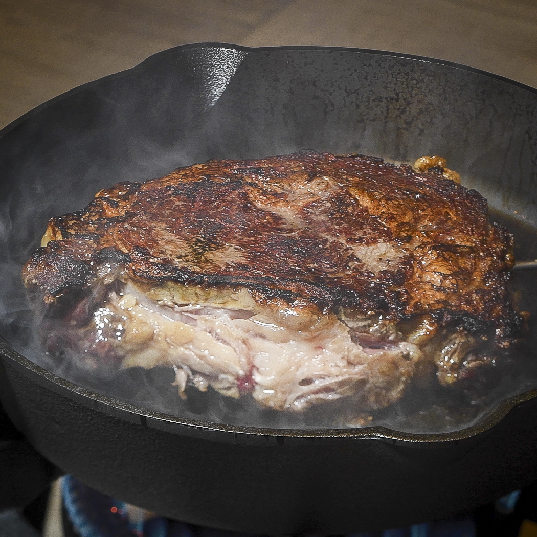 Ribeye cooking in a cast-iron skillet.