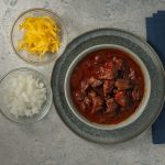 Texas Chili with cheddar cheese and diced onion.